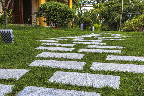Moderner Gartenweg aus großen Steinplatten, eingebettet in eine Rasenfläche.